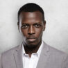 Portrait of successful confident dark-skinned entrepreneur wearing gray formal suit, standing against studio wall with copy space for your text or promotional content, looking serious and thoughtful